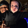 baby, adult, hoodie, indoor, smile, person, face, child, holding, warm_lighting, portrait, shelf, box, cozy, family, closeup, black_clothing, happy, casual, bonding