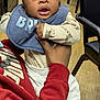 Amiri joined the competition — help win amazing prizes! baby, bib, child, indoor, person, hand, clothing, flooring, chair, furniture, expression, sleeve, sock, holding, adult, red_sweatshirt, blue_bib, wood_floor, curly_hair, open_mouth