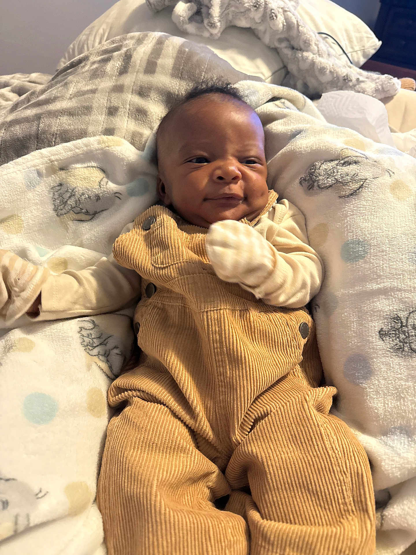 Amiri is registered to the contest to win money with this photo: baby, infant, corduroy_overalls, mittens, blanket, animal_print, soft_texture, indoor, cute, child, portrait, smile, relaxed, cozy, fabric, person, newborn, bed, comfort, young