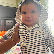 Noah James Alba is registered to the contest to win money with this photo: baby, infant, child, portrait, striped_outfit, sun_hat, smiling, sitting, supported, face, eyes, indoor, home, television, dresser, curtain, sunlight, colorful_blanket, bracelet, adorable