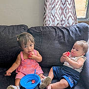 Isaac is registered to the contest to win money with this photo: toddler, child, watermelon, blue_bowl, pink_dress, navy_shorts, couch, indoor, curtain, window, shoes, fruit, food, sitting, cute, young, meal, snack, person, home