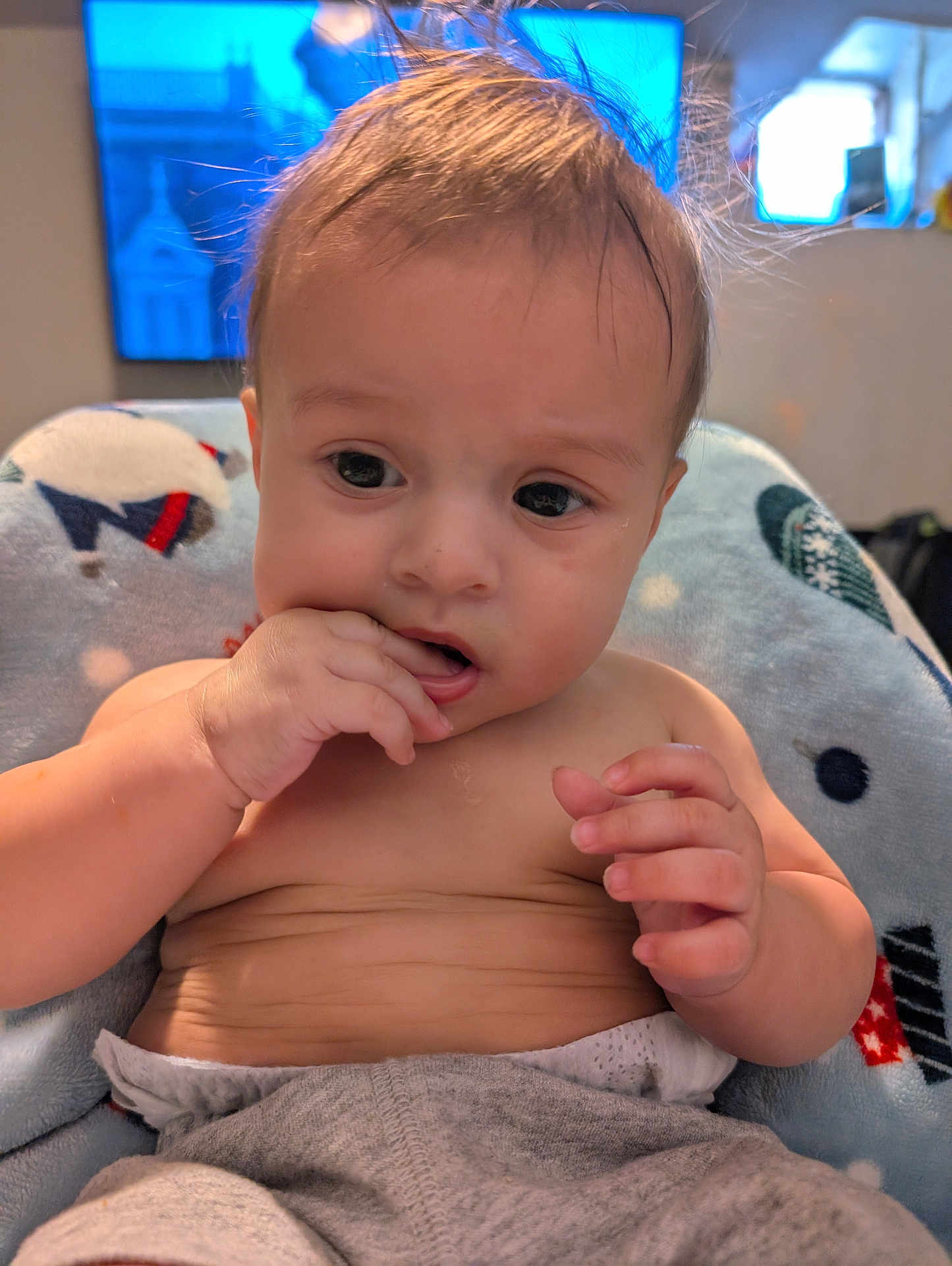 Isaac is registered to the contest to win money with this photo: baby, infant, hand, face, fingers, hair, blanket, clothing, diaper, sitting, indoors, television, expression, skin, cute, child, portrait, curious, cozy, home