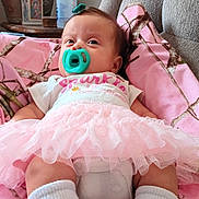Naomi is registered to the contest to win money with this photo: baby, pacifier, tutu, pink_blanket, white_socks, hair_clip, armchair, vase, table, indoor, child, cute, infant, clothing, comfort, portrait, relaxing, home, soft, cozy