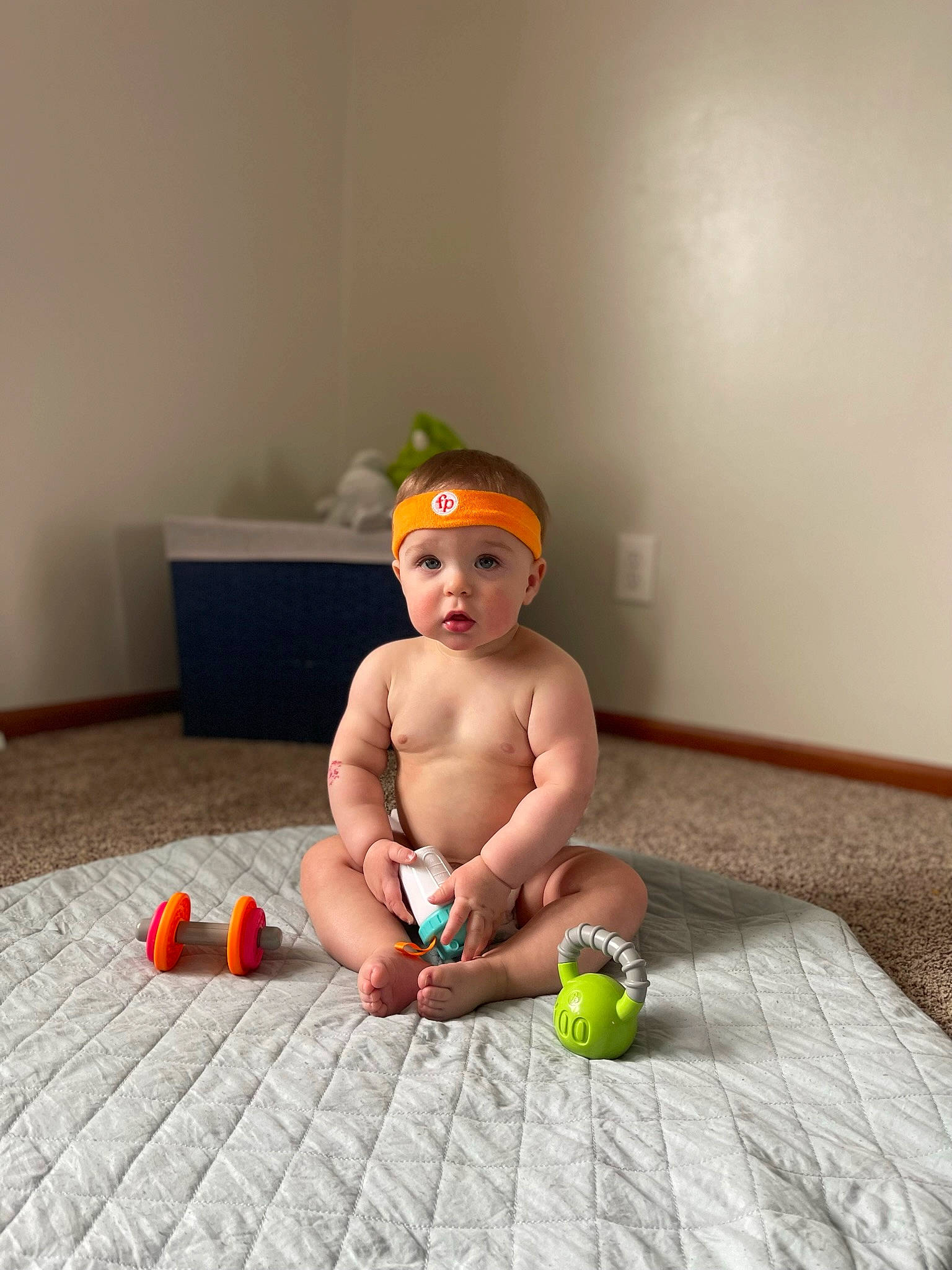 Collin is registered to the contest to win money with this photo: baby, baby_toys, ball, child, floor, flooring, foot, fun, hardwood, headwear, human_leg, knee, leisure, person, play, room, sandal, sitting, surprise, thigh