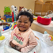 Alora is registered to the contest to win money with this photo: baby, smiling, child, toy, activity_center, bow, curly_hair, nursery, crib, colorful, playroom, infant, clothing, bib, happy, indoor, person, cute, seat, early_childhood