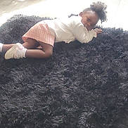 Passion is registered to the contest to win money with this photo: child, indoor, rug, floor, rocking_chair, plant_pot, wooden_chair, curly_hair, pink_skirt, white_shoes, socks, wood_floor, home, casual_clothing, relaxed, looking_at_camera, soft_lighting, black_rug, young_child, cozy