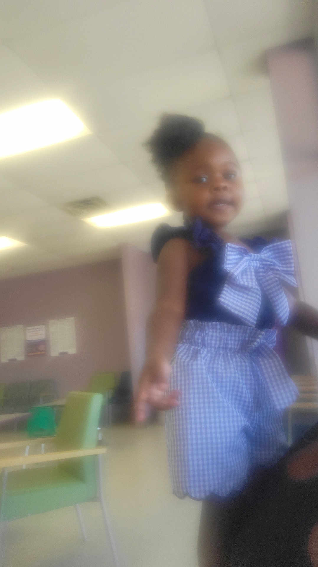 Passion is registered to the contest to win money with this photo: child, blurry, indoor, waiting_room, ceiling_lights, green_chair, checkered_outfit, bow, person, floor, table, wall, furniture, reaching_out, young_child, casual_clothing, hairstyle, room, light, portrait