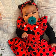 Kanova is registered to the contest to win money with this photo: baby, child, costume, ladybug, red, black, polka_dot, pacifier, headband, infant, cute, lying_down, blanket, clothing, portrait, indoors, sleeves, hand, face, expression