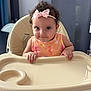 Serafina joined the competition — help win amazing prizes! baby, child, high_chair, pink_bow, curly_hair, seahorse_pattern, orange_clothing, indoor, table, hands, face, smile, person, headband, cute, infant, furniture, expression, skin, portrait