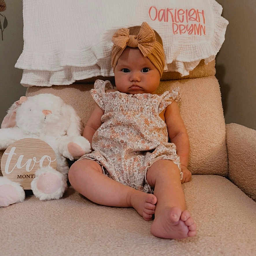 Oakleigh joined the competition — help win amazing prizes! baby, child, infant, armchair, stuffed_animal, bunny, headband, romper, fabric, textile, plush, person, portrait, indoor, seated, cute, expression, decor, name, cozy