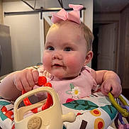 Oakleigh is registered to the contest to win money with this photo: baby, pink_bow, toy, activity_seat, indoor, child, cute, rosy_cheeks, playful, infant, colorful, smiling, person, portrait, hands, face, clothing, furniture, lighting, home