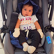 Zayn is registered to the contest to win money with this photo: baby, stroller, infant, mittens, blue_bonnet, white_socks, black_pants, colorful_shirt, face, child, tiled_floor, wheels, car_seat, cute, seated, indoors, expression, clothing, person, portrait