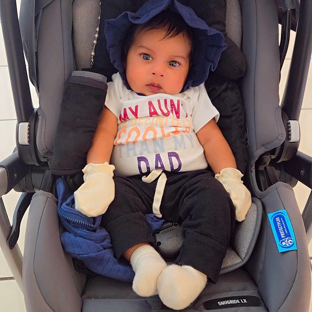 Zayn is registered to the contest to win money with this photo: baby, black_pants, blue_bonnet, car_seat, child, clothing, colorful_shirt, cute, expression, face, indoors, infant, mittens, person, portrait, seated, stroller, tiled_floor, wheels, white_socks