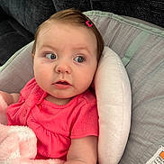 Annalise is registered to the contest to win money with this photo: baby, infant, pink_clothing, hair_clip, blanket, baby_seat, cushion, portrait, child, face, skin, indoor, comfort, curious, closeup, young_child, expression, soft_texture, seated, looking_away