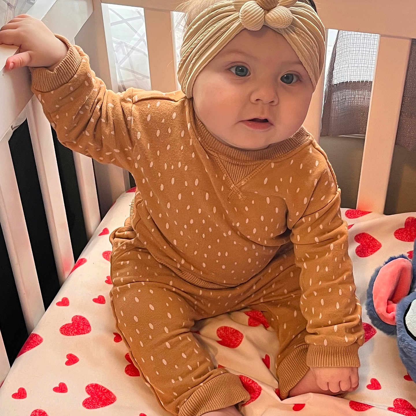 Annalise joined the competition — help win amazing prizes! baby, infant, crib, headband, brown_clothing, heart_pattern, bedding, window, curtains, indoors, child, cute, sitting, soft_light, cozy, foot, hand, face, person, nursery