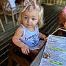 Hazel is registered to the contest to win money with this photo: toddler, child, blue_eyes, bow, hair_bow, high_chair, restaurant, menu, table, wooden_chair, indoor, curious, sitting, clothing, tank_top, person, face, young_child, cute, dining