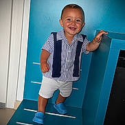 Kingsley participe au concours pour gagner de l'argent avec cette photo : toddler, child, smiling, blue_crocs, striped_shirt, white_shorts, bracelet, standing, indoors, staircase, railing, blue_wall, happy, person, footwear, short_sleeves, young_child, casual_clothing, portrait, cute