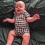 Eben is registered to the contest to win money with this photo: baby, child, smiling, romper, checkered_clothing, cushion, green, happy, sitting, plump, cute, infant, skin, face, legs, arms, indoors, comfortable, head, expression