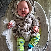 Eben is registered to the contest to win money with this photo: baby, infant, child, hooded_outfit, elephant_costume, baby_rocker, cushion, clothing, green_pants, striped_socks, flooring, indoor, smiling, cute, cozy, seat_belt, wood_floor, plush, person, portrait