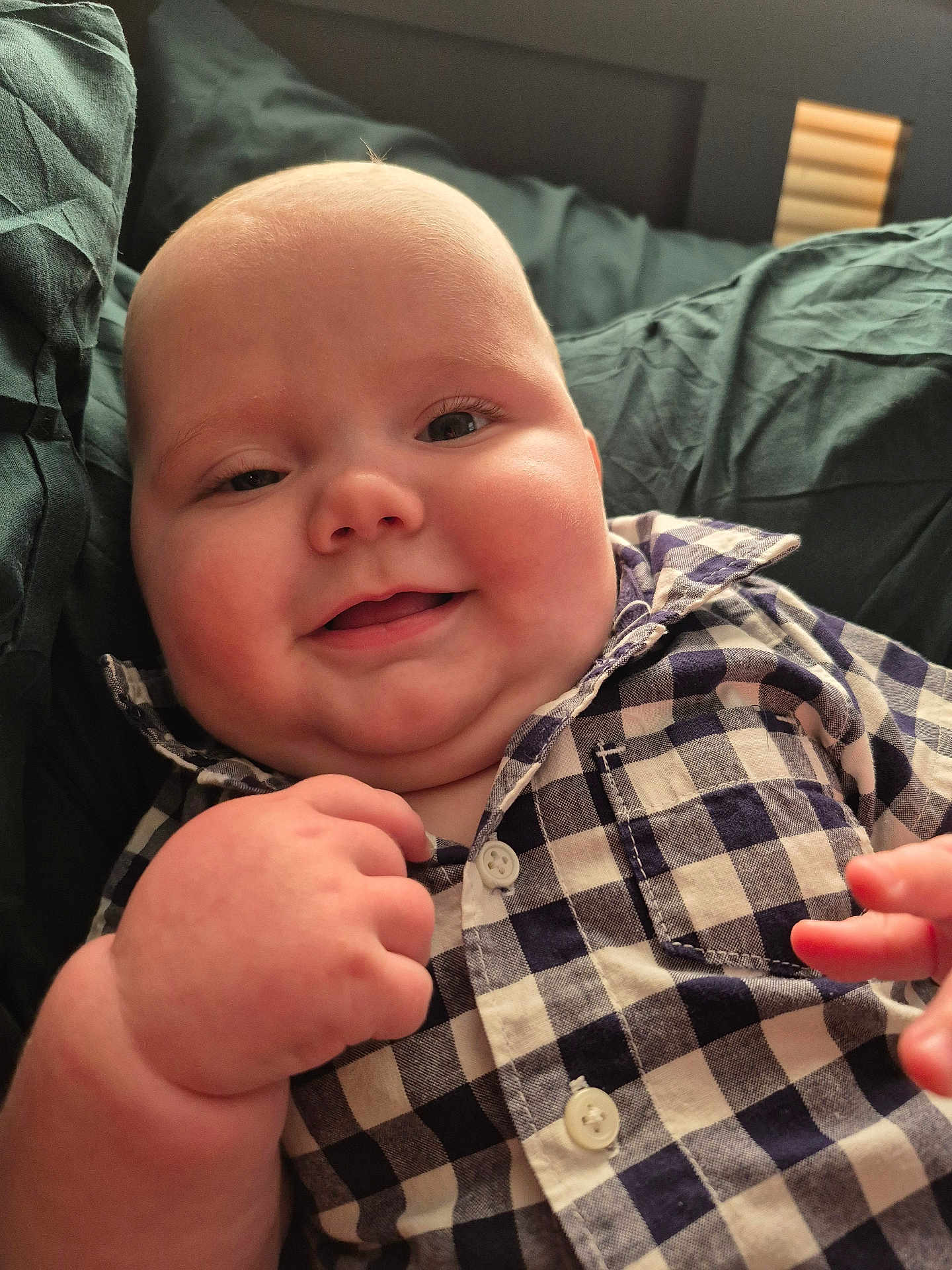 Eben is registered to the contest to win money with this photo: baby, smiling, face, cheeks, hand, shirt, checkered, clothing, infant, child, portrait, cute, happy, skin, fingers, person, closeup, soft, indoors, resting