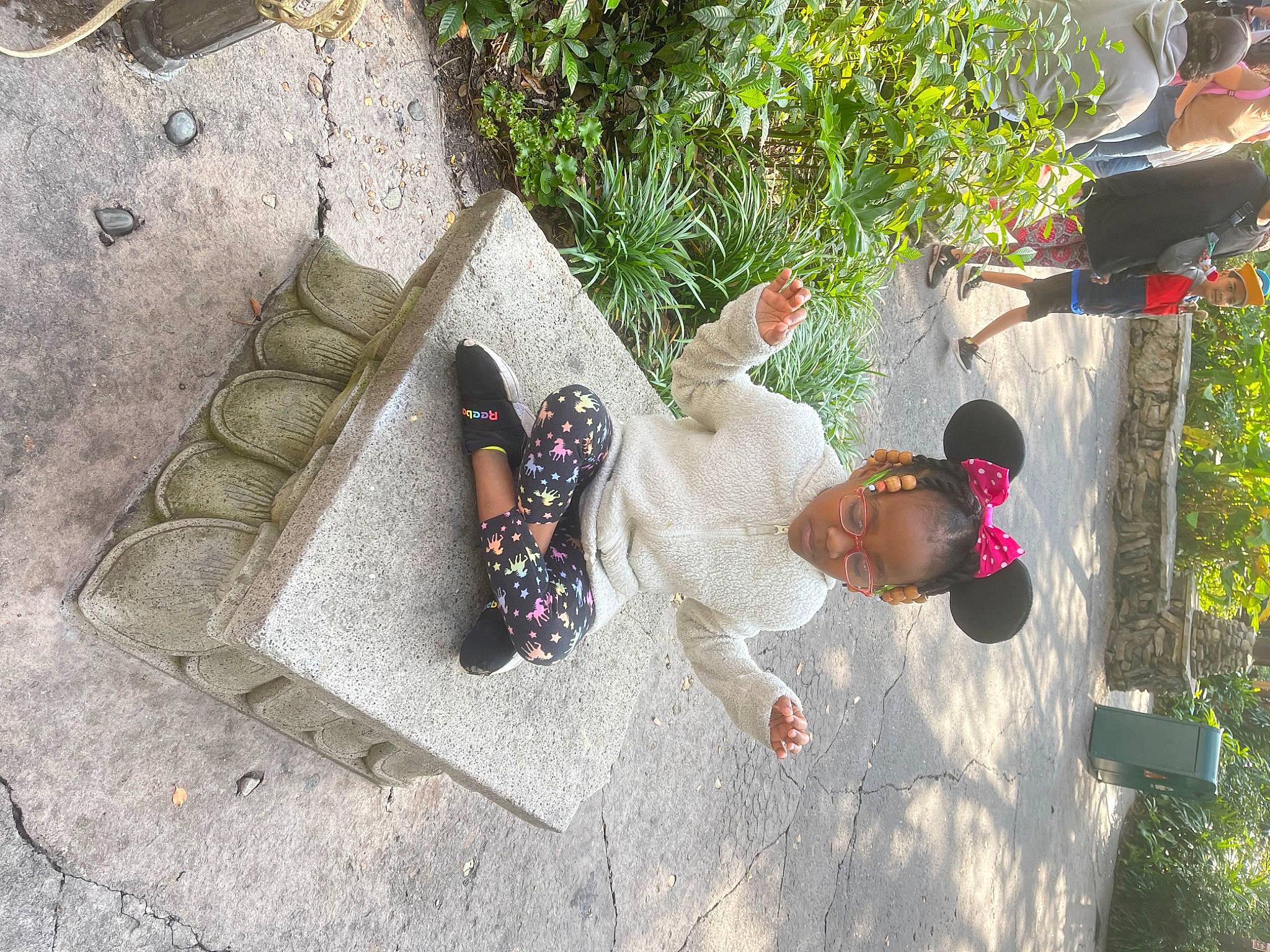 Cyan is registered to the contest to win money with this photo: concrete, fun, grass, headwear, leisure, person, plant, road_surface, rock, sandal, shadow, sidewalk, soil, toddler, tree