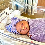 Liliana joined the competition — help win amazing prizes! newborn, baby, hospital, bassinet, blanket, headband, purple, wrapped, infant, sleeping, birth_record, towel, face, cute, person, indoors, lying_down, peaceful, swaddled, newborn_baby