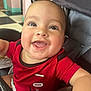 Uriyah is registered to the contest to win money with this photo: baby, smiling, red_shirt, stroller, child, happy, face, indoors, closeup, portrait, cute, infant, cheerful, seated, young_child, clothing, person, bright, expression, joy