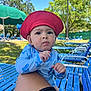 Uriyah is registered to the contest to win money with this photo: baby, child, red_hat, blue_outfit, shark_pattern, outdoor, lawn_chair, grass, trees, sunlight, summer, park, leg, person, nature, daylight, shade, blue_sky, relaxation, vacation