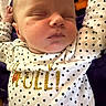 baby, sleeping, infant, onesie, polka_dot, white_clothing, gold_text, blanket, purple_blanket, orange_blanket, close_up, face, peaceful, resting, cute, newborn, soft_texture, child, portrait, indoor
