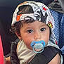 toddler, child, car_seat, pacifier, cap, hat, safety_belt, seatbelt, car_interior, curly_hair, cute, baby, young_child, looking, sitting, casual_clothing, colorful, indoors, portrait, vehicle