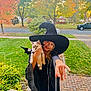 Sylvie joined the competition — help win amazing prizes! child, cat, witch_costume, black_hat, autumn, fall_leaves, porch, green_grass, trees, residential_street, smiling, costume, pet, outdoor, daylight, person, white_cat, reaching_hand, plants, sidewalk