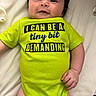 baby, infant, onesie, green_clothing, smiling, face, hand, lying_down, cute, child, text_on_clothing, indoor, skin, person, baby_clothes, portrait, human, white_background, young_child, playful