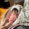 baby, infant, onesie, pink_stripes, baby_seat, cushion, face, hand, wooden_floor, indoor, patterned_bedding, animal_ears, cute, child, person, relaxing, furniture, floor, skin, portrait