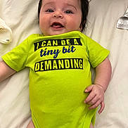 Maelani Cardenas joined the competition — help win amazing prizes! baby, infant, smiling, clothing, green_onesie, text_on_clothing, lying_down, bed, white_sheet, hand, face, child, cute, happy, portrait, skin, infant_clothing, young_child, indoors, person