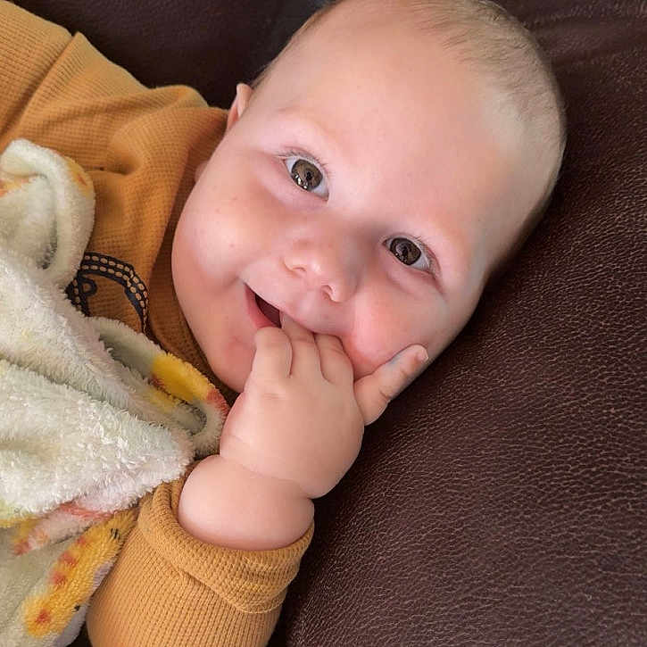 Matthew is registered to the contest to win money with this photo: baby, blanket, child, clothing, couch, cozy, cute, eyes, face, fingers, hand, happy, indoor, infant, leather, portrait, relaxed, skin, smiling, young