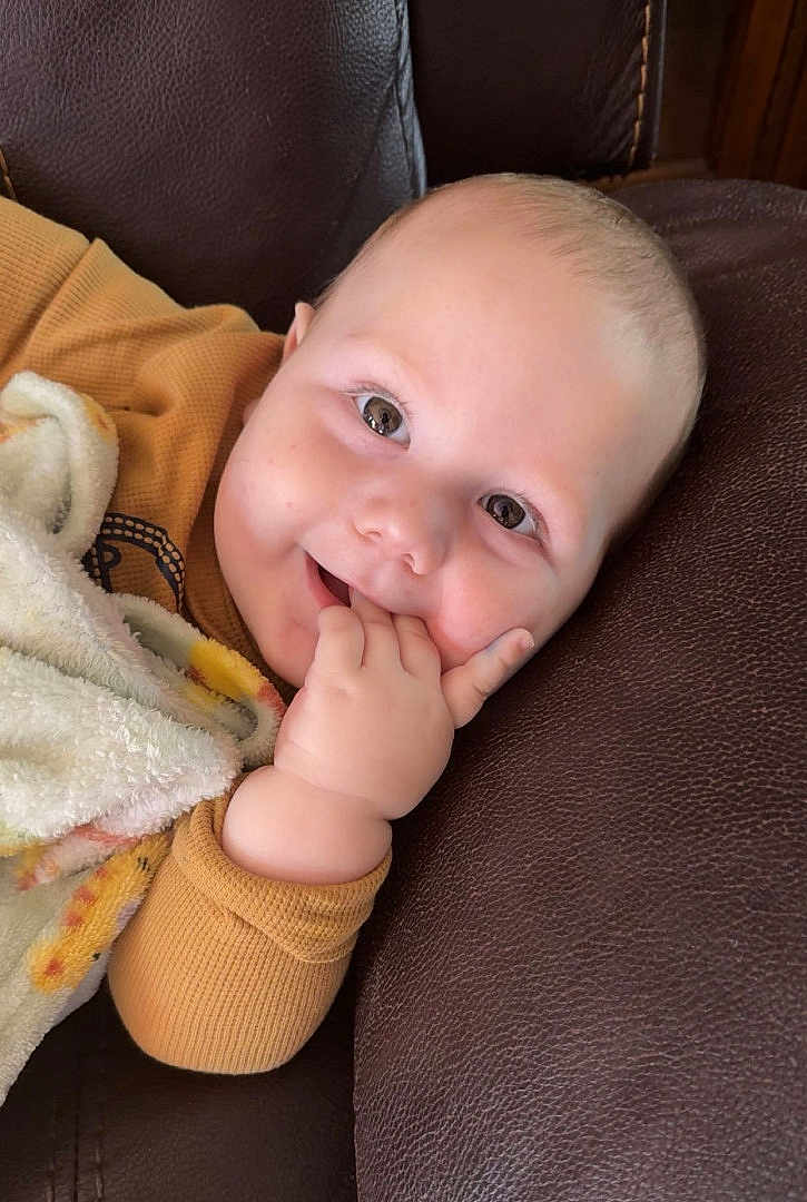 Matthew is registered to the contest to win money with this photo: baby, smiling, infant, blanket, couch, leather, hand, face, eyes, clothing, cute, child, portrait, cozy, indoor, relaxed, skin, happy, fingers, young
