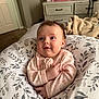 Elizabeth joined the competition — help win amazing prizes! baby, infant, pink_onesie, floral_pattern, pillow, bedroom, furniture, dresser, blanket, carpet, smile, face, child, person, indoors, cute, happy, cozy, soft_lighting, home