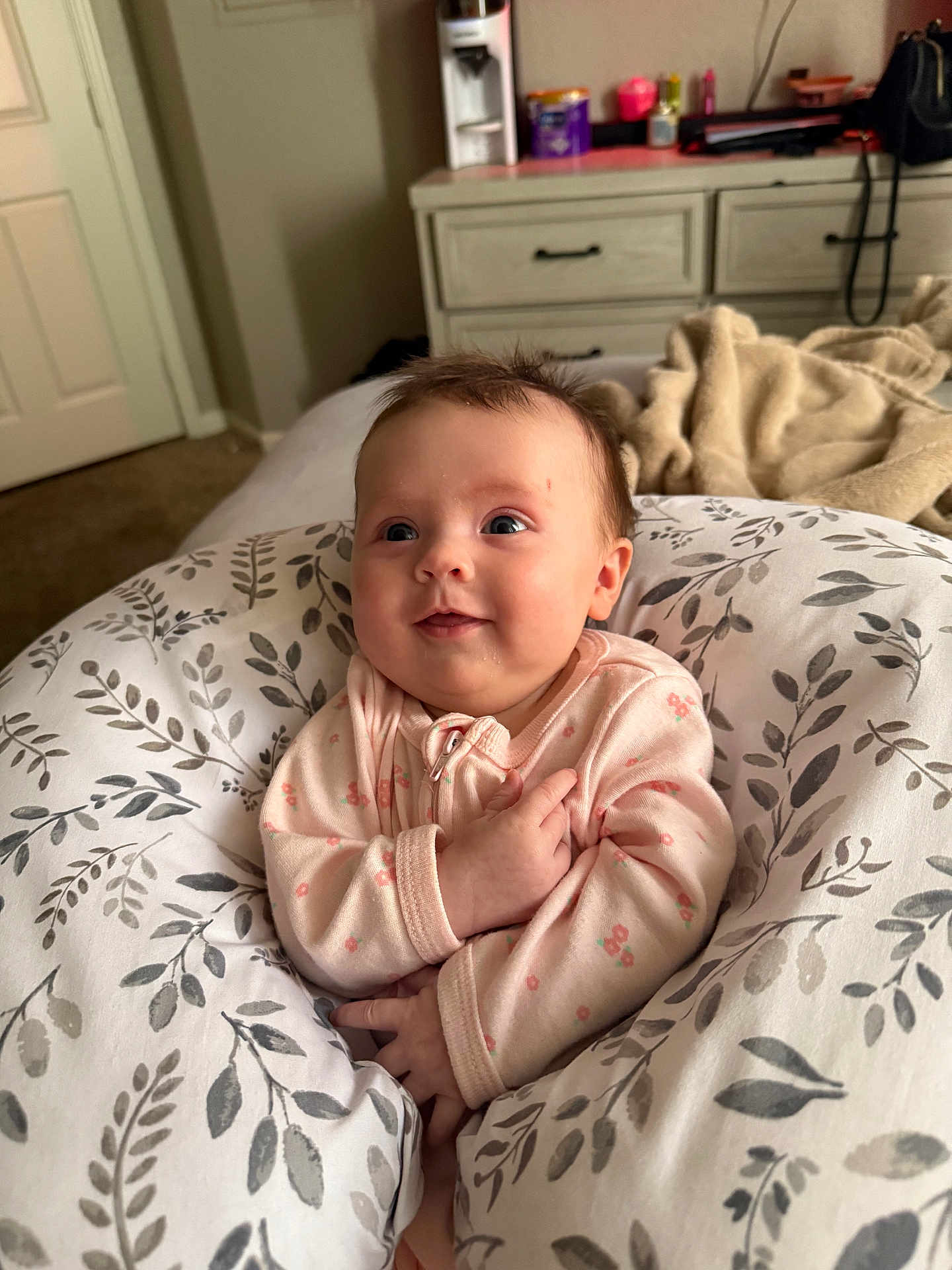 Elizabeth joined the competition — help win amazing prizes! baby, infant, pink_onesie, floral_pattern, pillow, bedroom, furniture, dresser, blanket, carpet, smile, face, child, person, indoors, cute, happy, cozy, soft_lighting, home