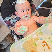 Oliver is registered to the contest to win money with this photo: baby, birthday, cake, celebration, child, curious, cute, face, food, frosting, hand, hat, high_chair, indoor, messy, person, seat, smudged, table, toddler