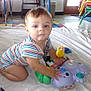 baby, child, toy, blanket, striped_clothing, floor, indoor, table, chair, window, door, colorful, play, kneeling, curious, person, floor_mat, plastic_toy, light, room
