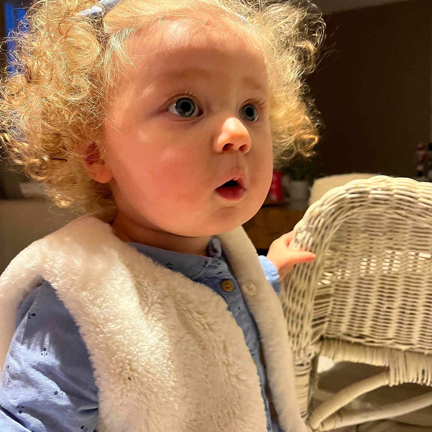 Alba a rejoint le concours — aidez-le/la à gagner de superbes lots ! blonde_hair, blue_eyes, blue_shirt, child, clothing, curious_expression, curly_hair, cute, face, furniture, hairclip, hand, indoor, person, portrait, soft_texture, toddler, vest, warm_light, wicker_chair