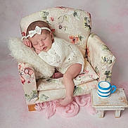 Mia joined the competition — help win amazing prizes! baby, sleeping, infant, knitwear, headband, bow, miniature_chair, floral_pattern, pillow, small_table, striped_cup, pink_background, cozy, cute, peaceful, indoor, portrait, newborn, soft_texture, resting