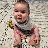 Axel participe au concours pour gagner de l'argent avec cette photo : arms, baby, barefoot, bed, bedspread, bib, child, cute, face, happy, head, indoors, infant, legs, pattern, person, sitting, skin, smiling, toy