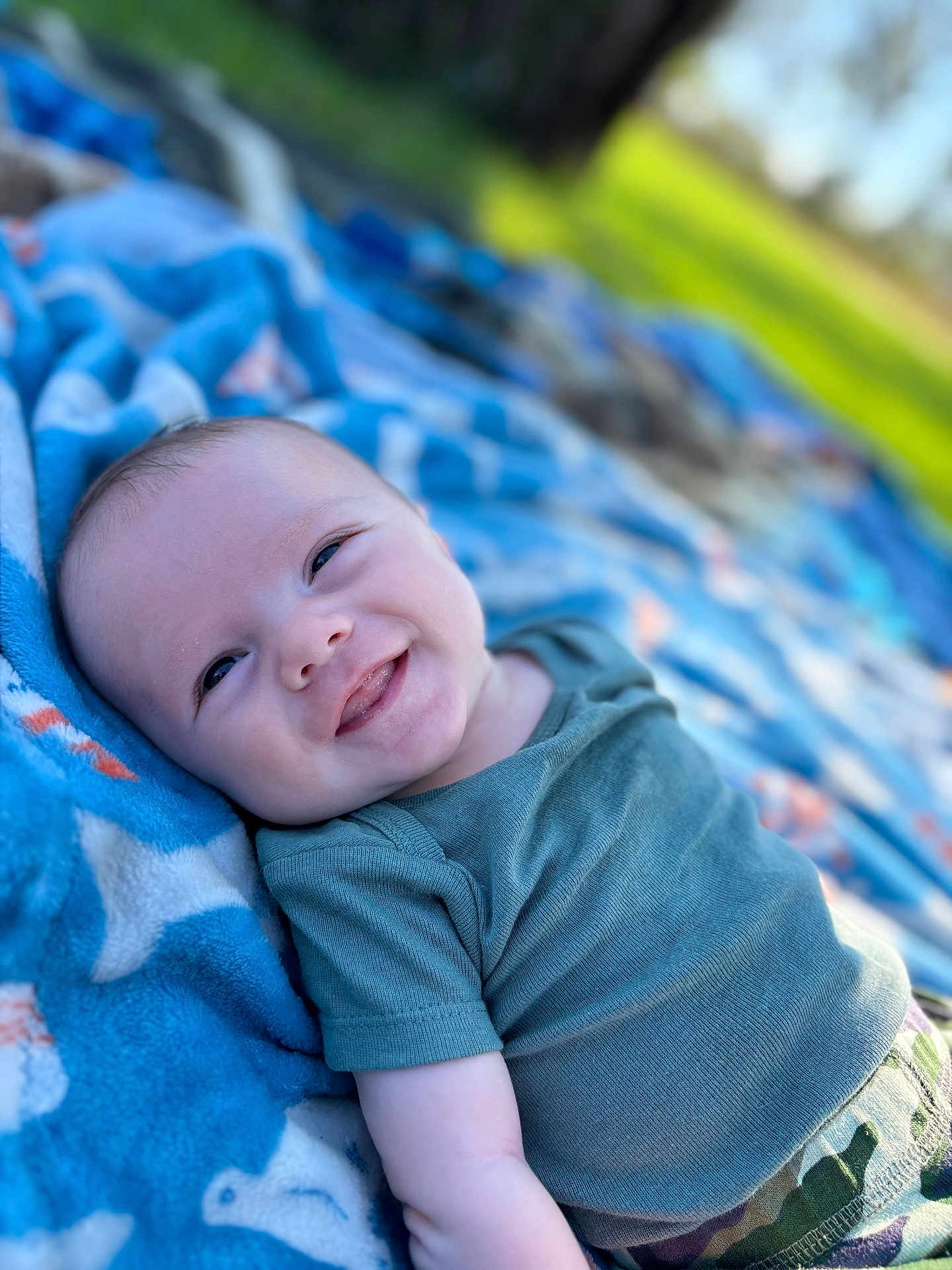 Cyrus joined the competition — help win amazing prizes! baby, smiling, infant, blanket, outdoor, green_shirt, camouflage_pants, face, happy, lying_down, child, nature, grass, sunlight, portrait, cute, person, blue_blanket, relaxing, daytime