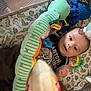 Cyrus is registered to the contest to win money with this photo: baby, infant, playpen, toy, plush_toy, blanket, dinosaur_pattern, clothing, face, eyes, hand, fabric, soft_toy, indoor, child, person, cute, lying_down, colorful, nursery