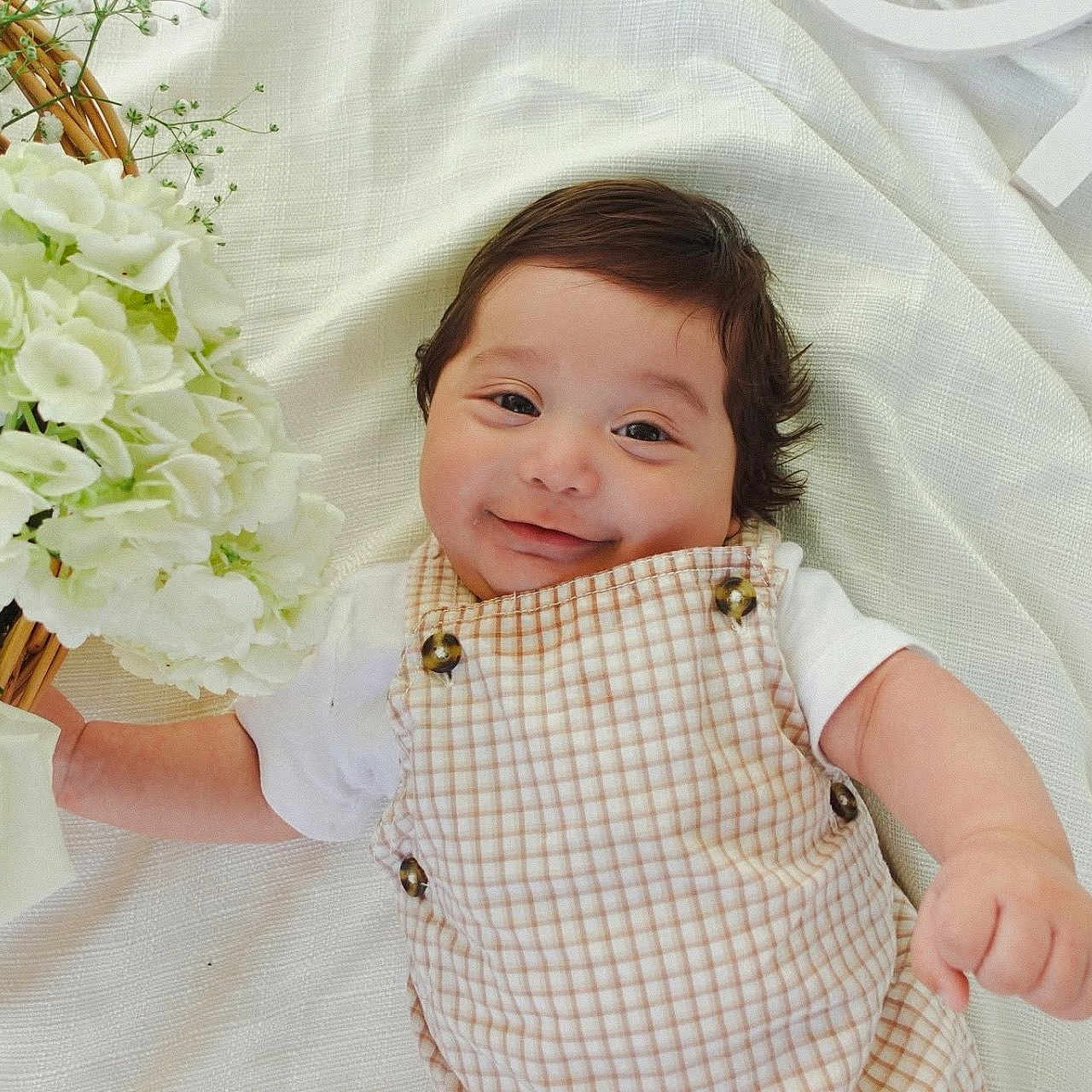 Noah is registered to the contest to win money with this photo: baby, basket, blanket, buttoned_overall, checkered_outfit, child, closeup, cute, decor, flower, happy, indoors, infant, lying_down, portrait, small_hand, smiling, soft_lighting, white_flower, young_child