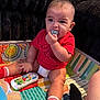 baby, infant, child, red_shirt, diaper, red_socks, toy_remote, plush_toy, play_mat, chewing, indoor, couch, colorful, cute, sitting, person, young_child, face, hand, foot