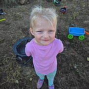 Oakley is registered to the contest to win money with this photo: bicycle, blond_hair, blue_eyes, child, dirt, dog, girl, grass, helmet, leggings, nature, outdoor, pink_shirt, play, scooter, shoes, smile, sunlight, toys, wagon