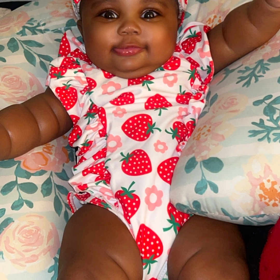 Riley is registered to the contest to win money with this photo: baby, bonnet, cap, clothing, couch, cushion, dress, face, furniture, happy, hat, head, homedecor, hood, person, photography, portrait, sitting, smile, swimwear