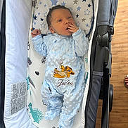Jules a rejoint le concours — aidez-le/la à gagner de superbes lots ! baby, newborn, onesie, blue_clothing, baby_carrier, cushion, simba_embroidery, hand_near_mouth, wooden_floor, stroller, dinosaur_print, star_print, infant, cute, sleepwear, indoor, portrait, cozy, child, relaxing